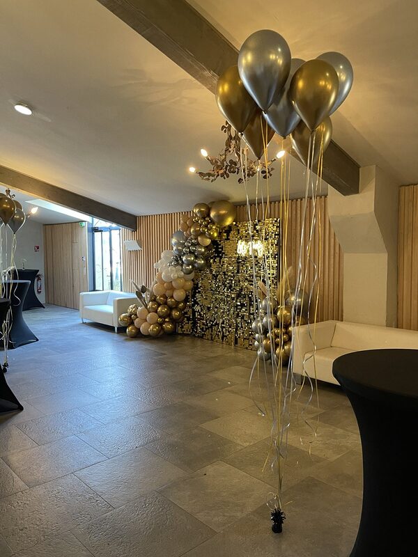 Hall du domaine : backdrop à sequins or entre deux canapés blancs, ballons or et argent à l’hélium et mange-debout housés de noir
