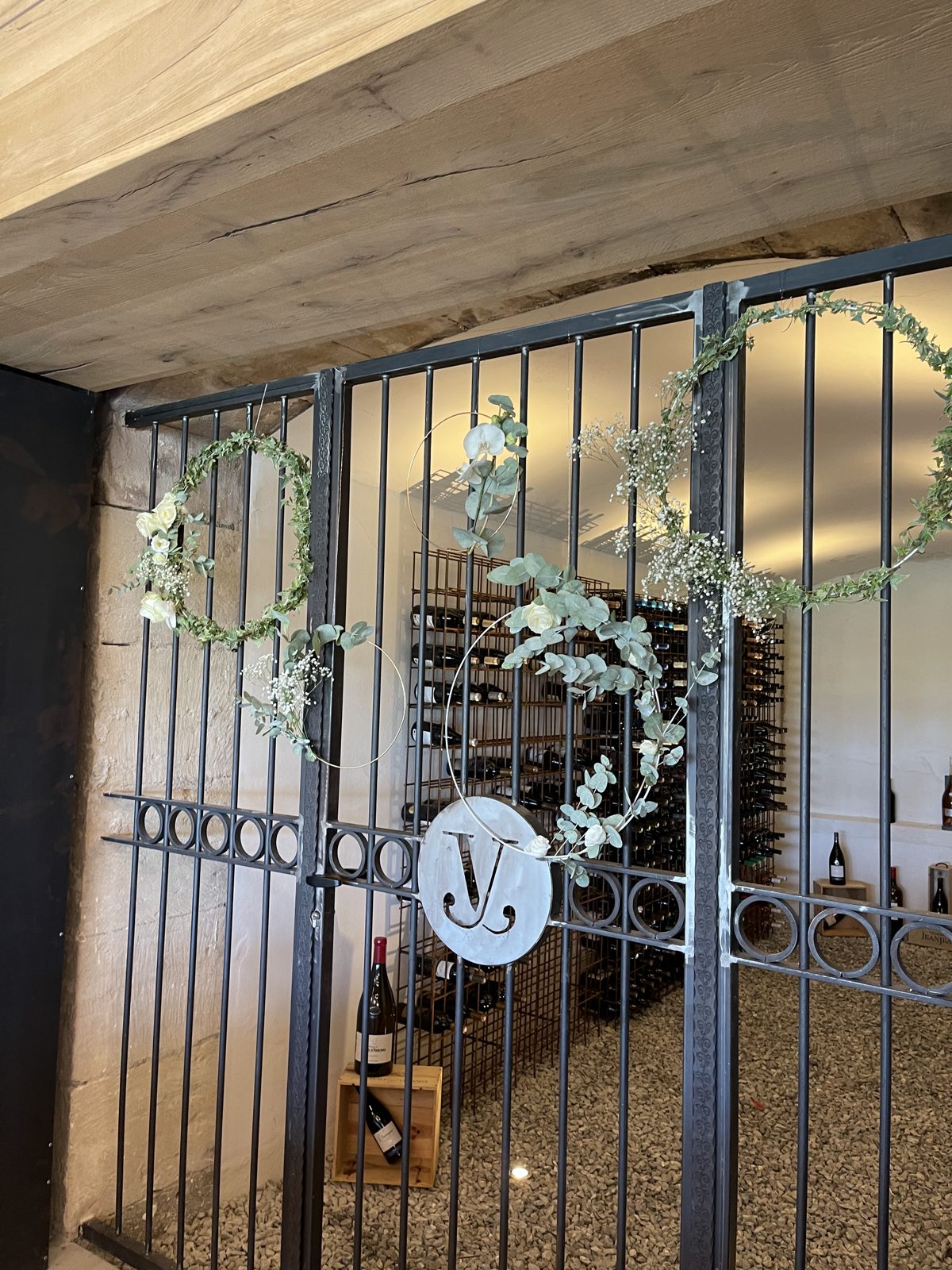 Grille de cave à vin ornée de couronnes d’eucalyptus, de gypsophile et de fleurs blanches, caisse en bois au sol