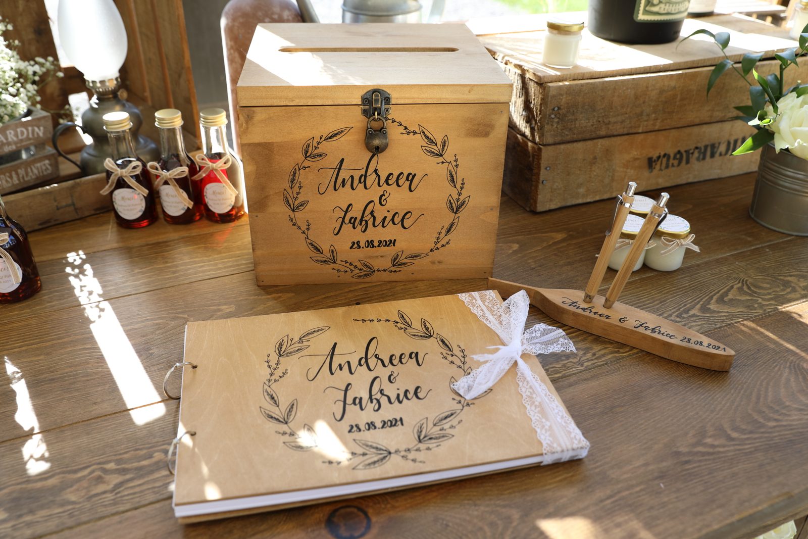 Urne en bois gravée et livre d’or en bois assorti sur une table, avec petites fioles en verre et caisses en bois