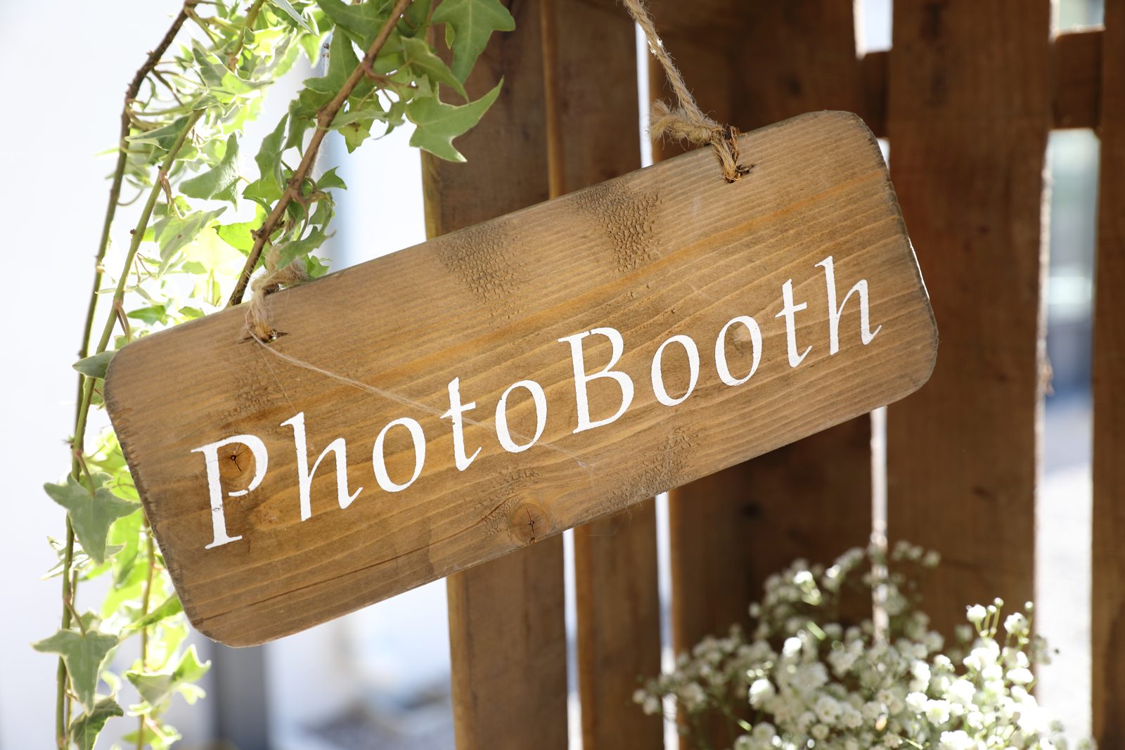 Pancarte en bois « PhotoBooth » suspendue par une corde à une palette, lierre et gypsophile tout autour