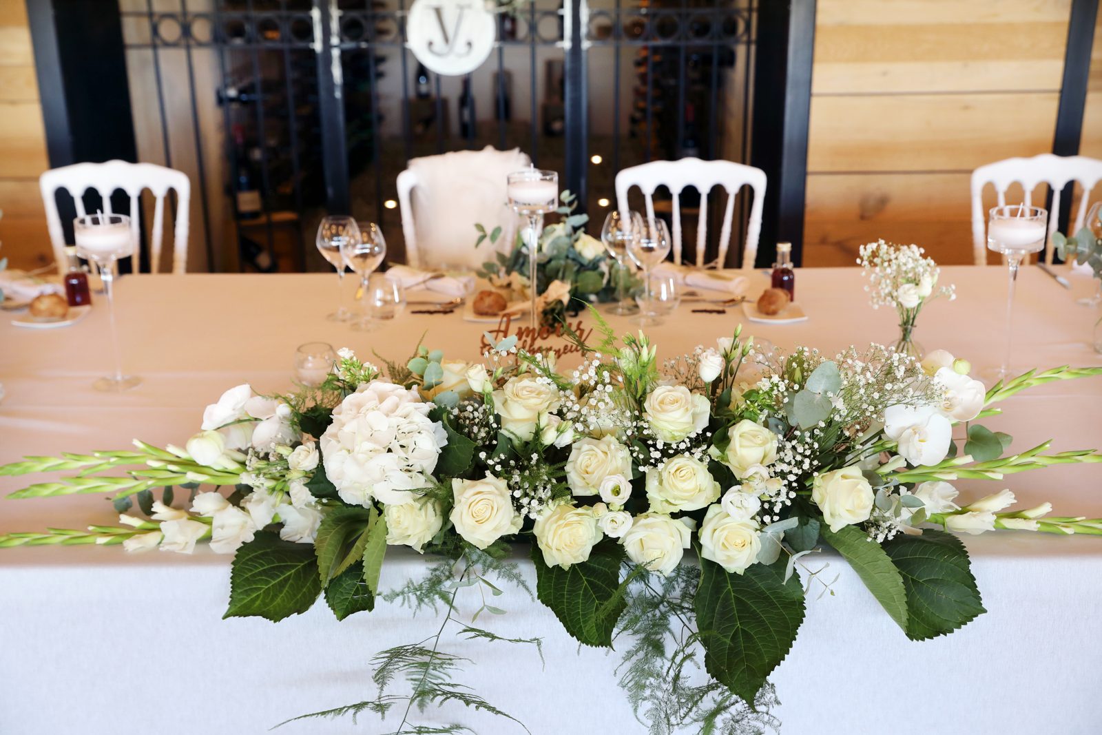 Longue composition de roses blanches, gypsophile et glaïeuls sur la table d’honneur, chaises Napoléon III blanches