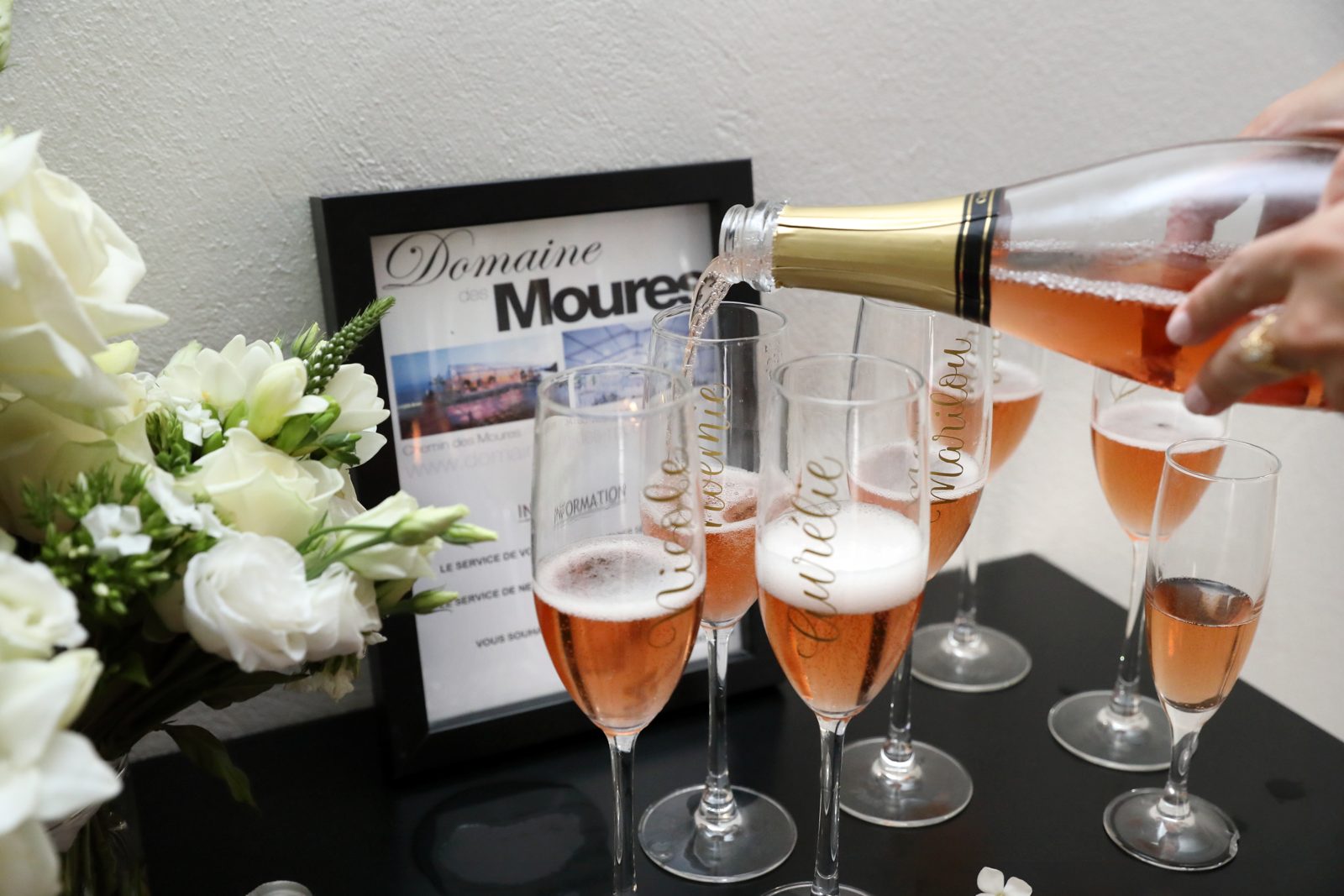 Service du champagne rosé dans des flûtes personnalisées, à côté d’un bouquet de roses blanches