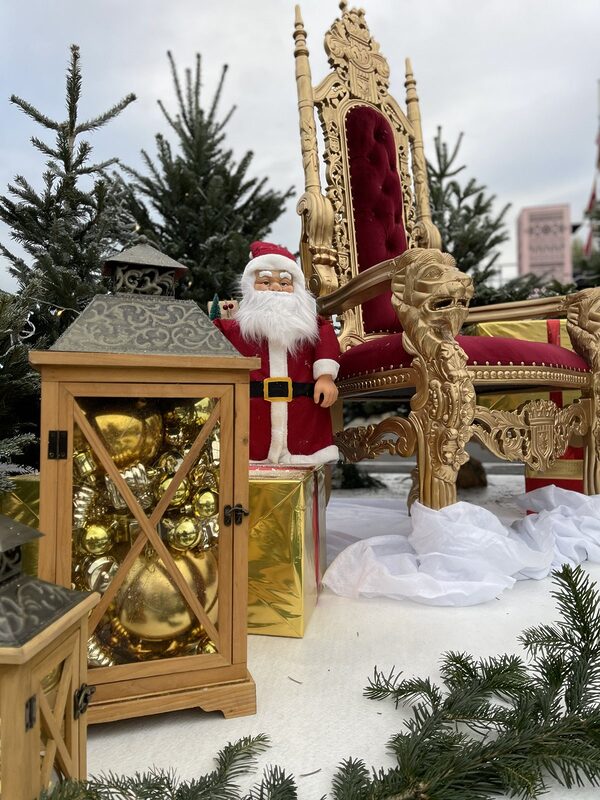 Lanterne en bois garnie de boules dorées et petit Père Noël au pied du trône doré