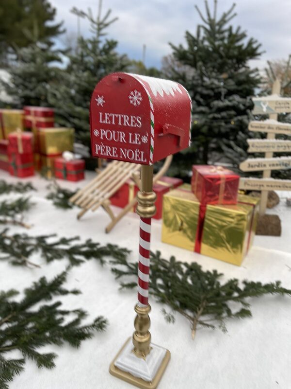 Boîte aux lettres rouge « Lettres pour le Père Noël » sur pied rayé, cadeaux et luge en arrière-plan