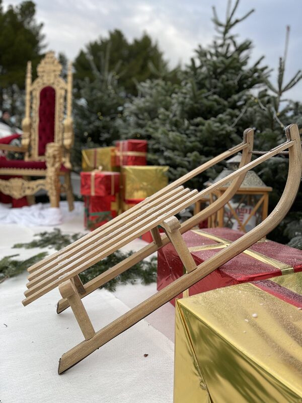 Luge en bois appuyée sur un cadeau doré, trône et sapins givrés flous en fond