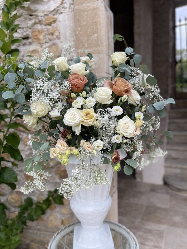 Arche en bois de bouleau drapée de voile terracotta, compositions de roses crème et caramel, gypsophile et eucalyptus, deux chaises médaillon blanches, mur de pierre