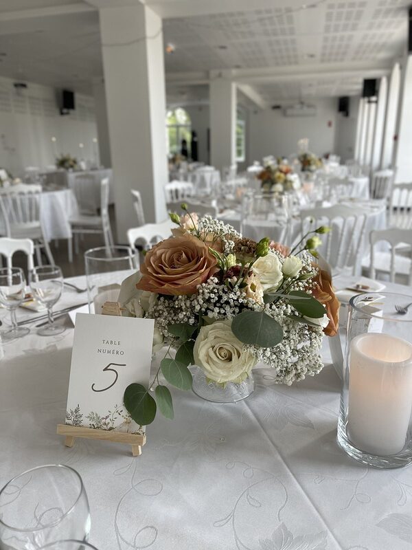 Centre de table de roses caramel et crème, gypsophile et eucalyptus, numéro de table sur petit chevalet en bois et bougie LED dans un vase cylindre