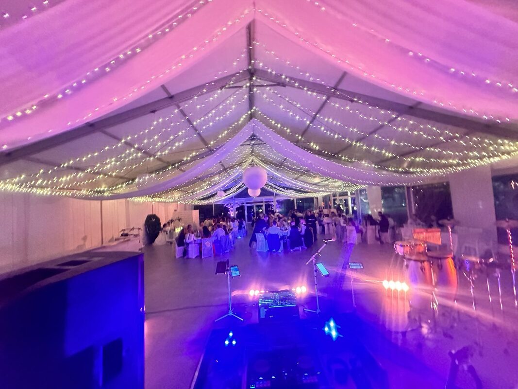 Chapiteau vu depuis la scène : drapés d’organza tendus et guirlandes lumineuses en lignes au-dessus des tables rondes