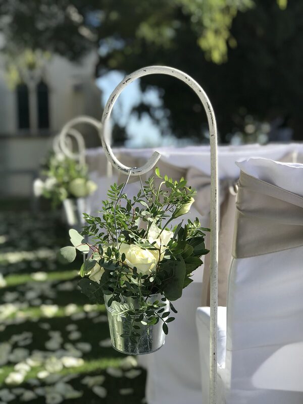 Crochet de berger blanc portant un petit seau en zinc garni de roses blanches et de feuillage, le long de l’allée