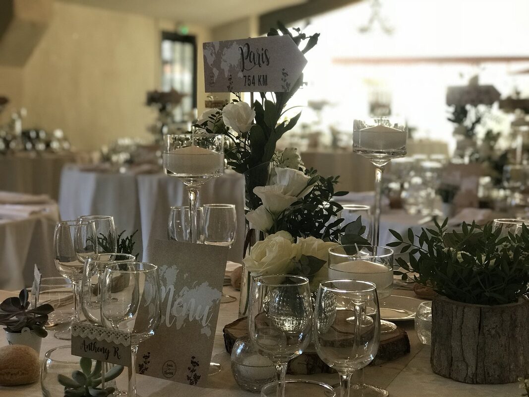 Tables rondes nappées de blanc, bougies flottantes sur pied et compositions de roses blanches, pot en écorce garni de pistachier