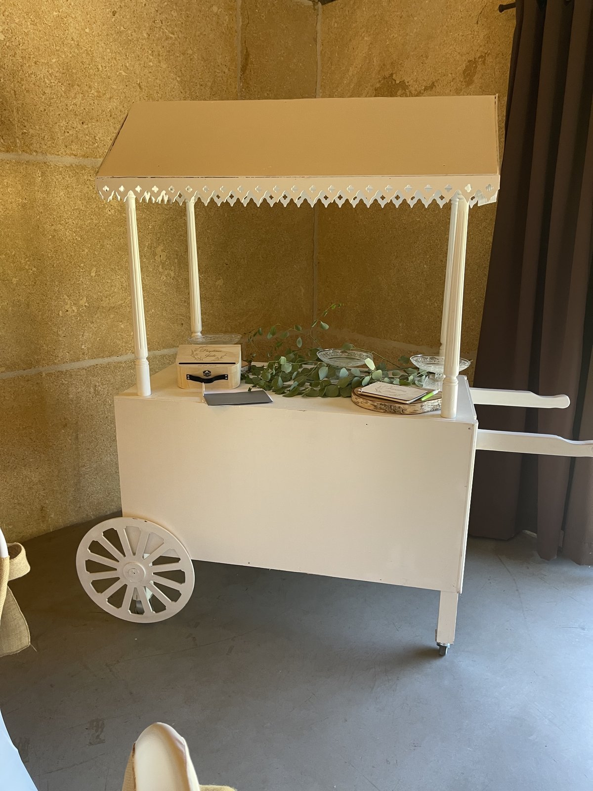 Charrette de candy bar en bois blanc à auvent festonné, garnie d’eucalyptus, d’un coffret en bois et de coupelles
