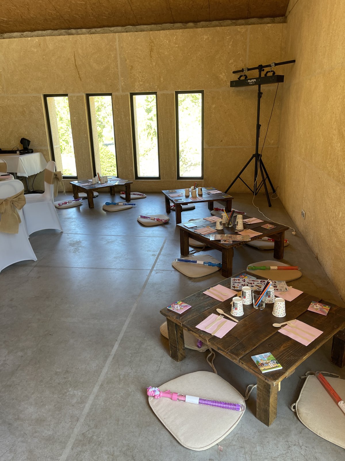 Coin enfants dans une salle en pierre : tables basses en bois sombre, galettes au sol, gobelets et cahiers de coloriage