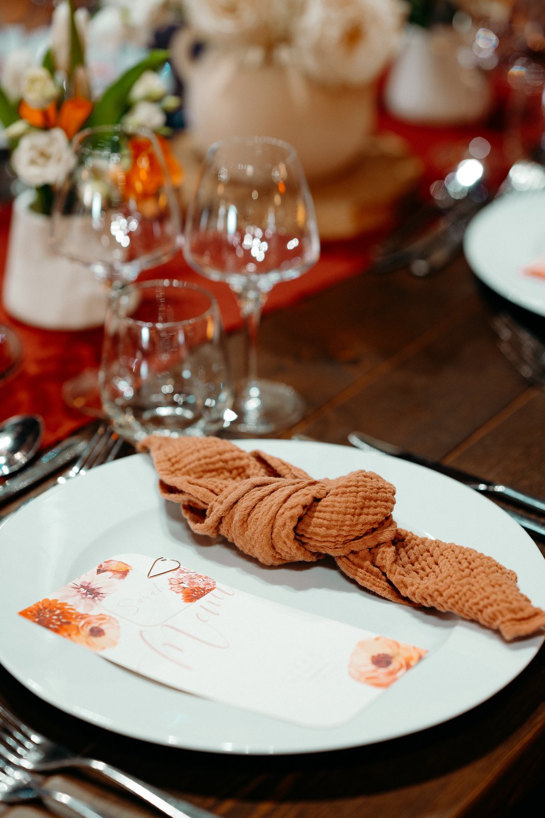 Serviette en gaze de coton caramel nouée sur une assiette blanche avec un menu illustré de fleurs orange