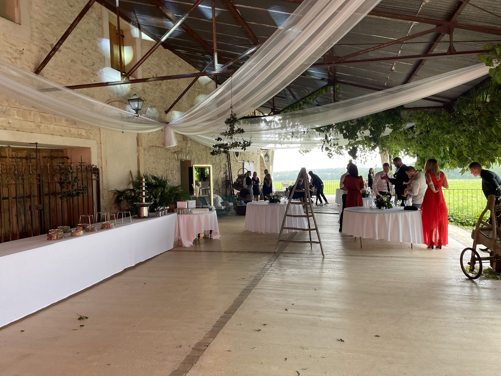 Halle couverte drapée de voile blanc, buffet en nappes blanches, tables rondes et échelle décorative pour le cocktail