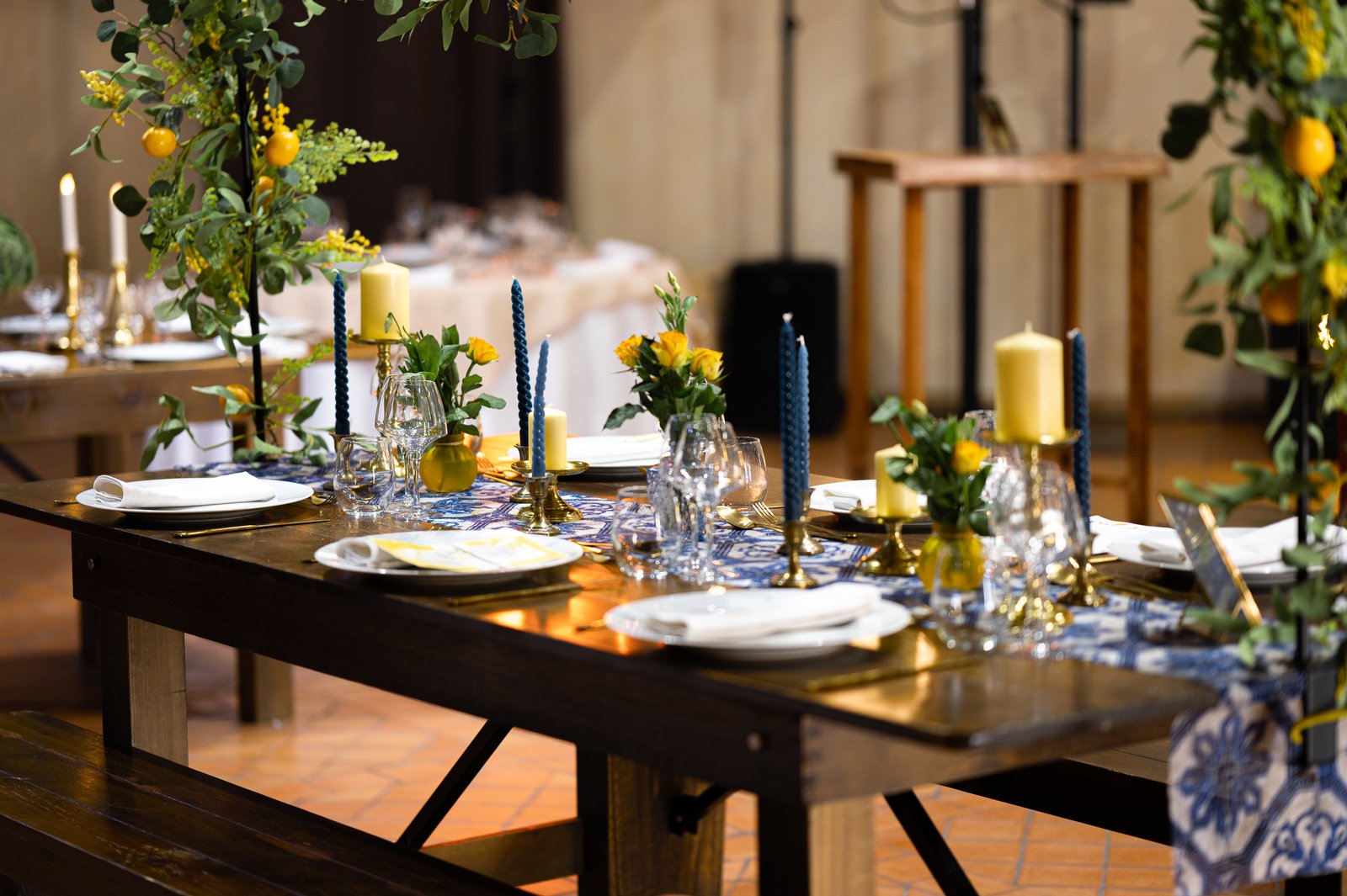 Tablée en bois dressée sur un chemin de table azulejos, bougies torsadées bleues, bougeoirs en laiton et roses jaunes