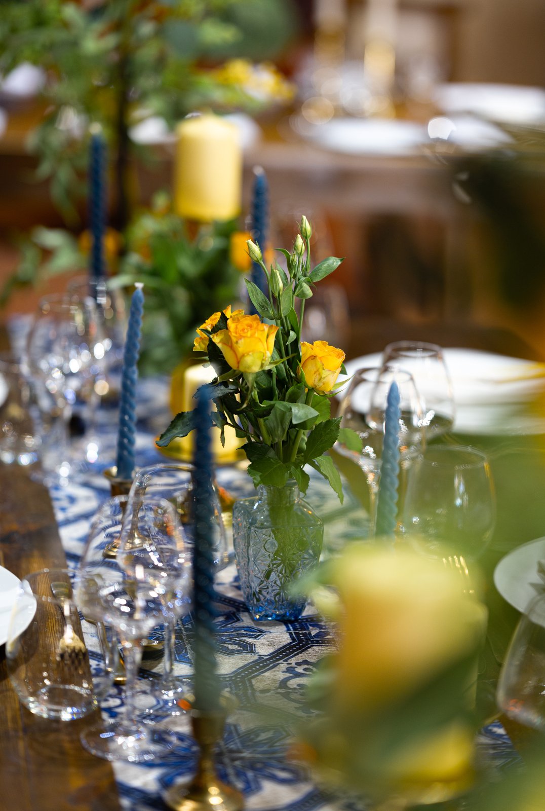 Petits bouquets de roses jaunes, bougies torsadées bleu nuit et bougie jaune sur un chemin de table bleu et blanc