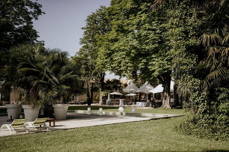 Parc arboré d’un domaine avec bassin où flottent des boules lumineuses, tentes blanches et mobilier de réception en fond
