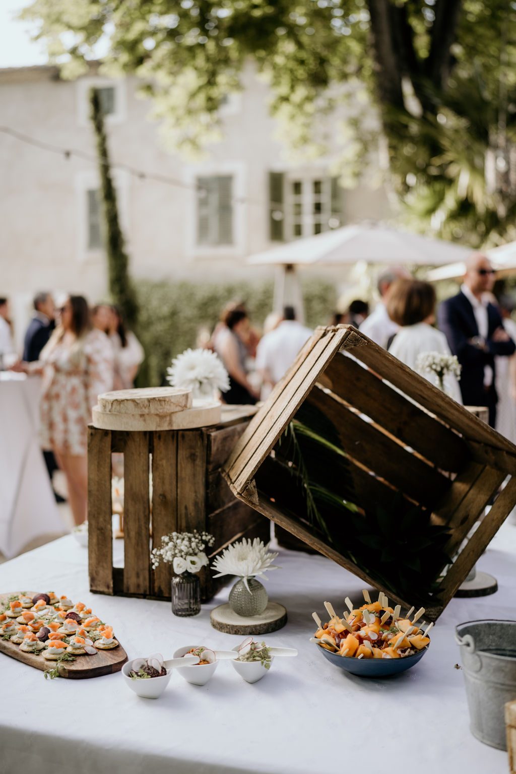Buffet de cocktail en plein air : caisses en bois, petits vases de fleurs blanches, planches de bouchées et verrines