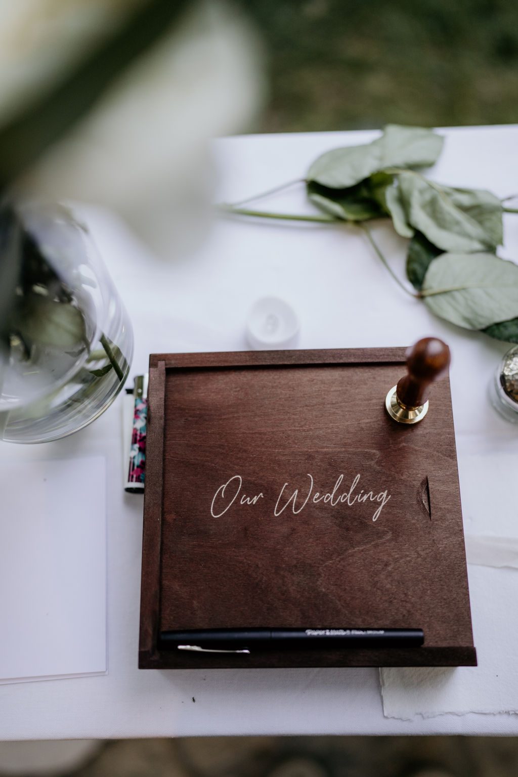 Coffret en bois gravé posé sur une table blanche avec tampon à cachet, feutre et feuillage d’eucalyptus
