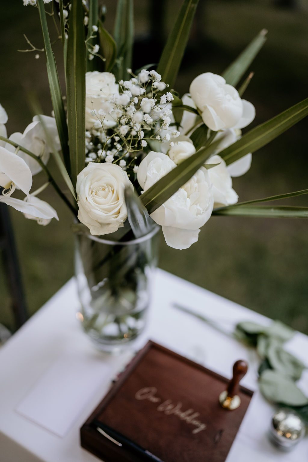 Vase en verre de roses blanches, gypsophile et feuillage sur une table blanche, coffret en bois gravé au premier plan