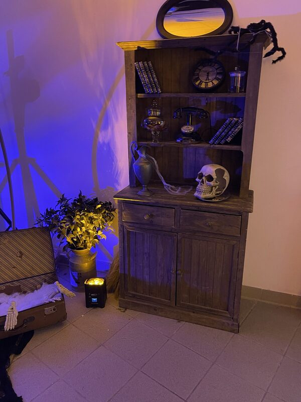 Buffet en bois garni de vieux livres, horloge, téléphone vintage, bonbonnière et crâne, araignée géante et miroir ovale