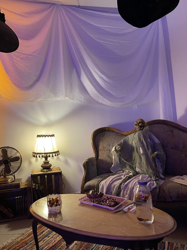 Le salon hanté sous un voilage tendu, lumière orange et violette, spectre sur le canapé vintage