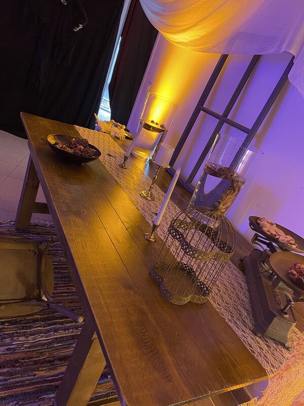 Table en bois au chemin de dentelle, chandeliers et bougies LED, cage à oiseaux vintage, vases cylindres aux mains flottantes, lumière ambrée
