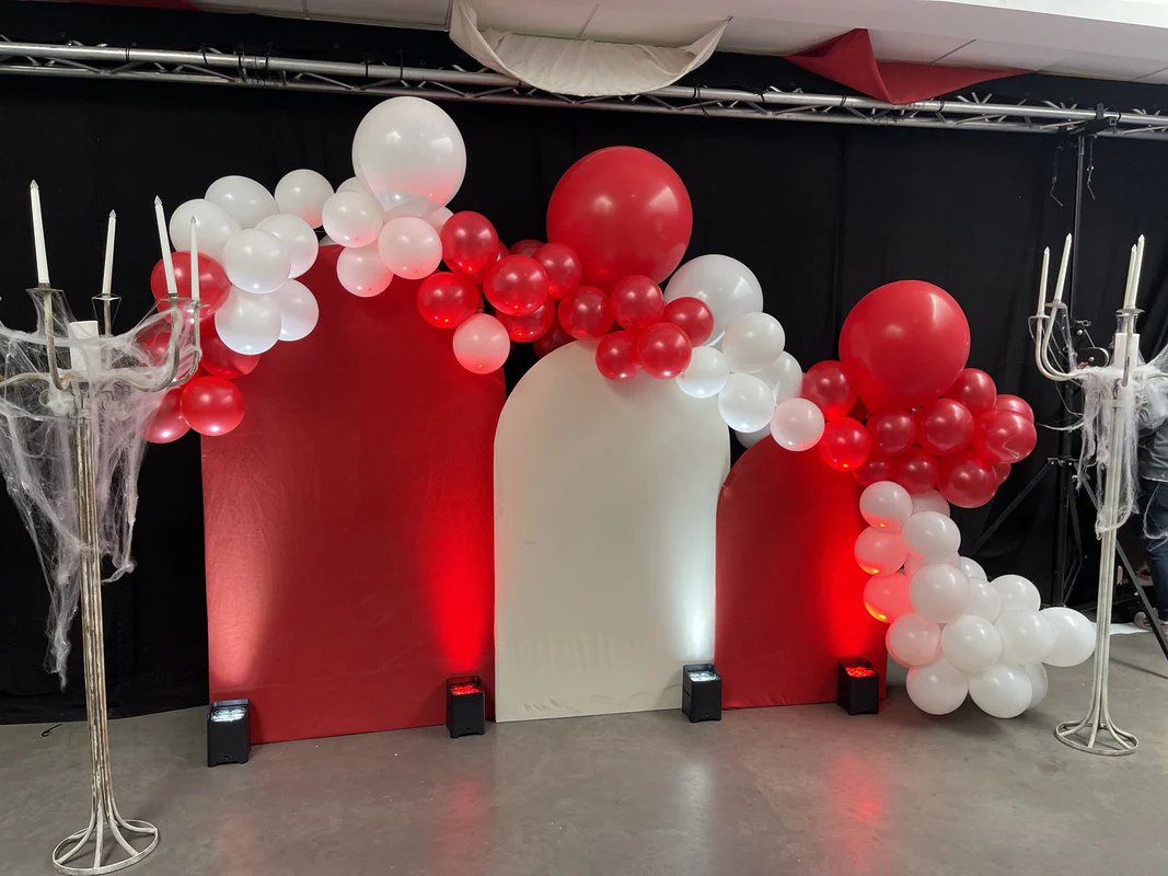 Arche en tissu rouge et blanc et guirlande de ballons rouges et blancs, encadrée de deux chandeliers blancs couverts de toiles d’araignée