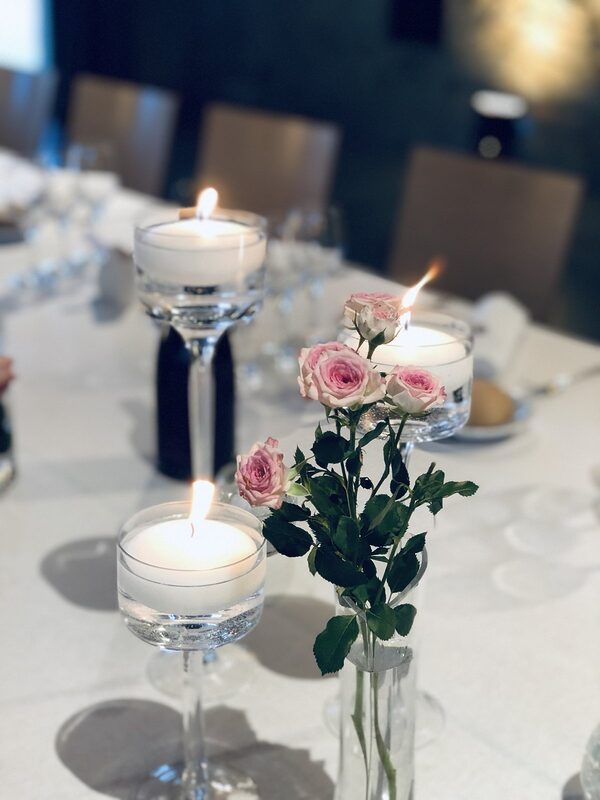 Bougies flottantes allumées dans des vases sur pied et petites roses roses en soliflore, sur une table nappée de blanc