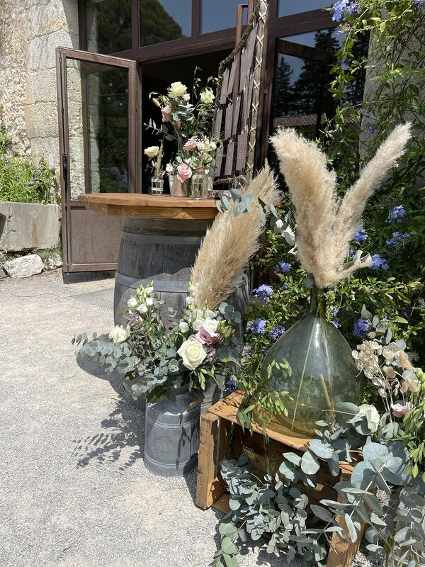 Composition de pampas, roses blanches et eucalyptus dans un bidon en zinc et une dame-jeanne posée sur une caisse en bois