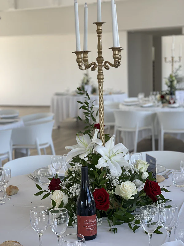 Chandelier doré à cinq branches et bougies blanches au-dessus d’une composition de roses rouges, roses blanches et lys