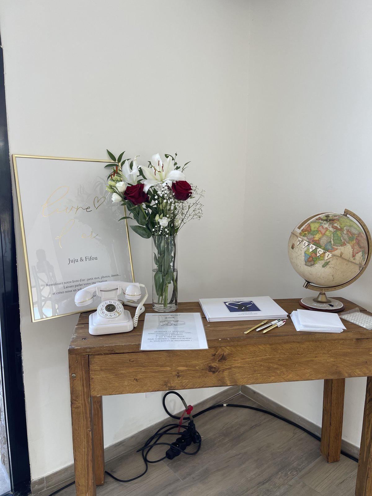Console en bois avec téléphone blanc de livre d’or audio, cadre doré, vase de roses rouges et de lys, globe terrestre
