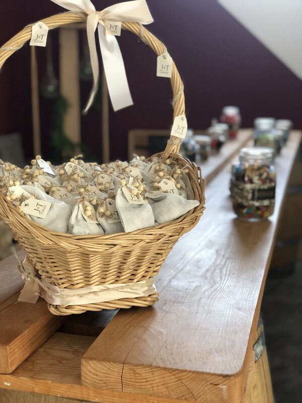 Panier en osier garni de petits sachets de dragées en lin, sur un bar en bois