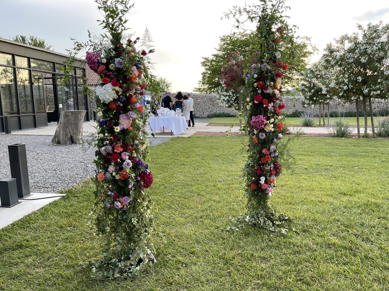 Arche florale ouverte en deux colonnes de fleurs rouges, roses et blanches mêlées de verdure, sur la pelouse d’un domaine