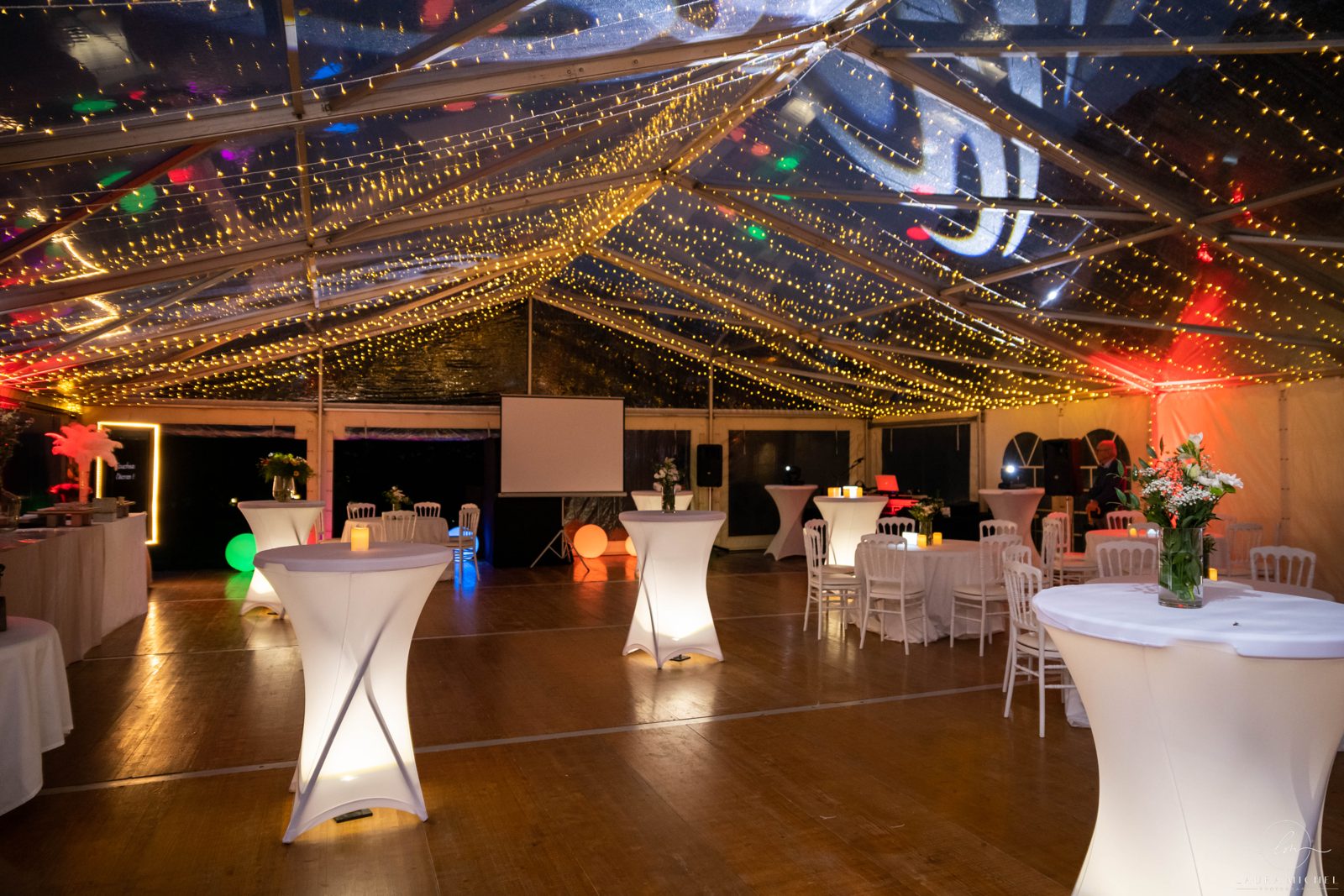Chapiteau cristal de nuit sous un ciel de guirlandes lumineuses, mange-debout lumineux housés de lycra et chaises blanches