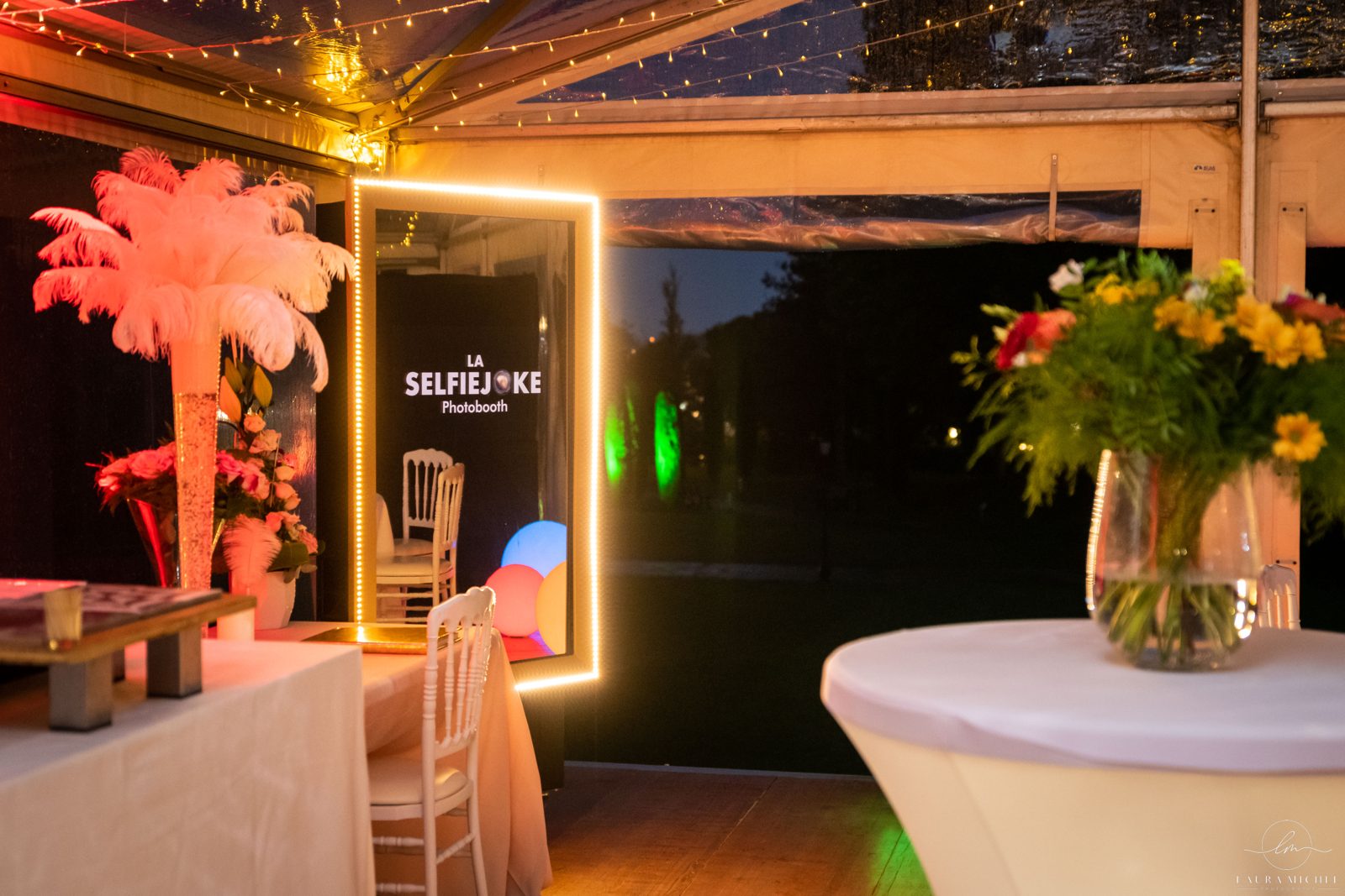 Borne photo miroir lumineuse, vase flûte à plumes d’autruche, mange-debout housé de blanc et bouquet de fleurs jaunes