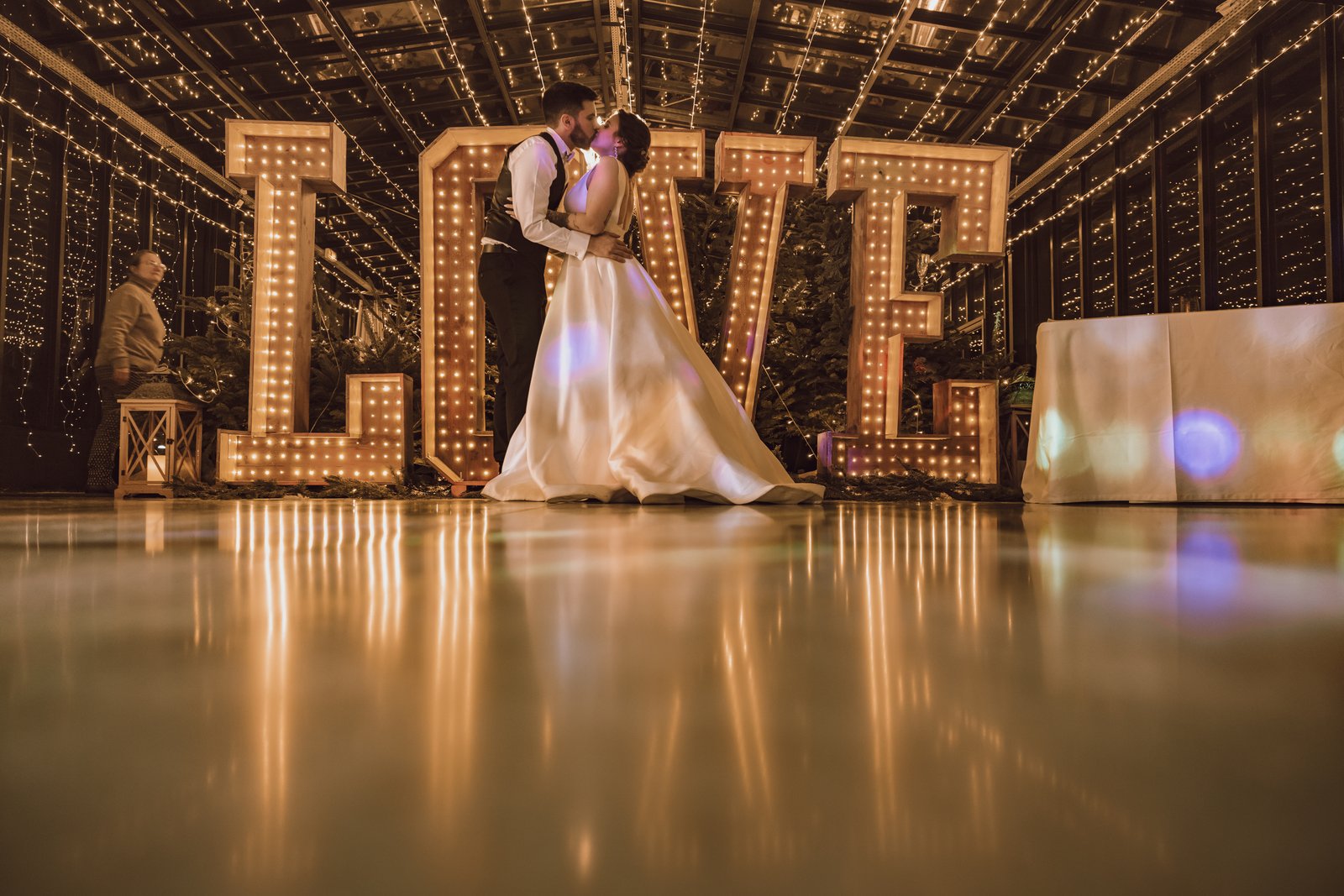 Les mariés devant les lettres LOVE géantes en bois illuminées, sur une piste brillante sous un plafond de guirlandes