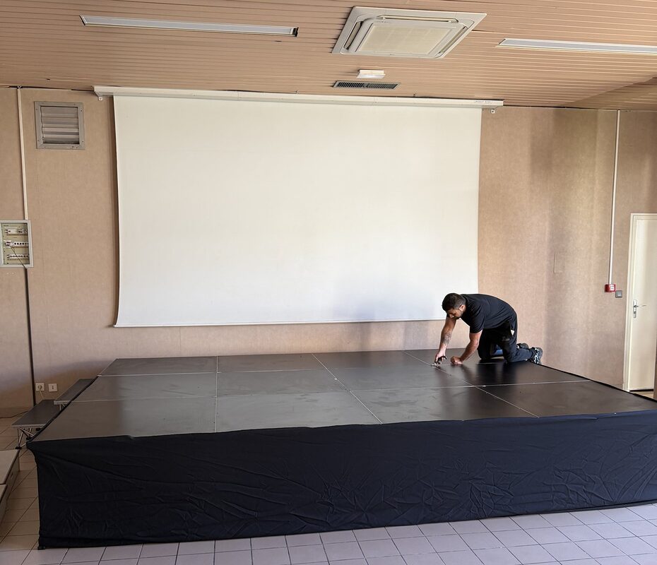 Praticables de scène Pink Event en cours de montage dans une salle, devant l'écran de projection