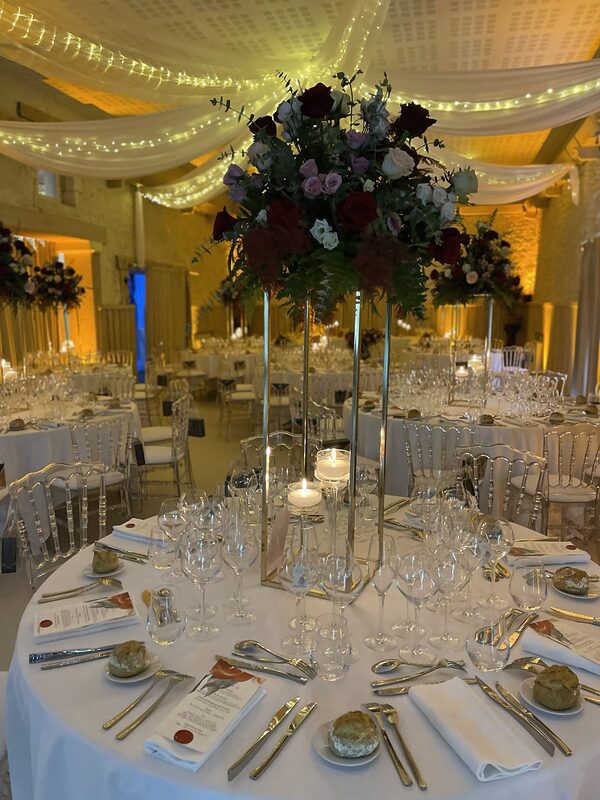 Centre de table de roses rouges, mauves et blanches sur une colonne dorée, bougies flottantes sur pied, chaises Napoléon III cristal