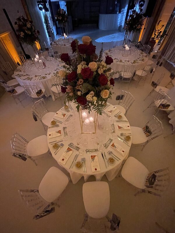 Table ronde vue du dessus, chaises Napoléon III cristal, centre de table fleuri sur colonne dorée et bougies flottantes, lumière tamisée