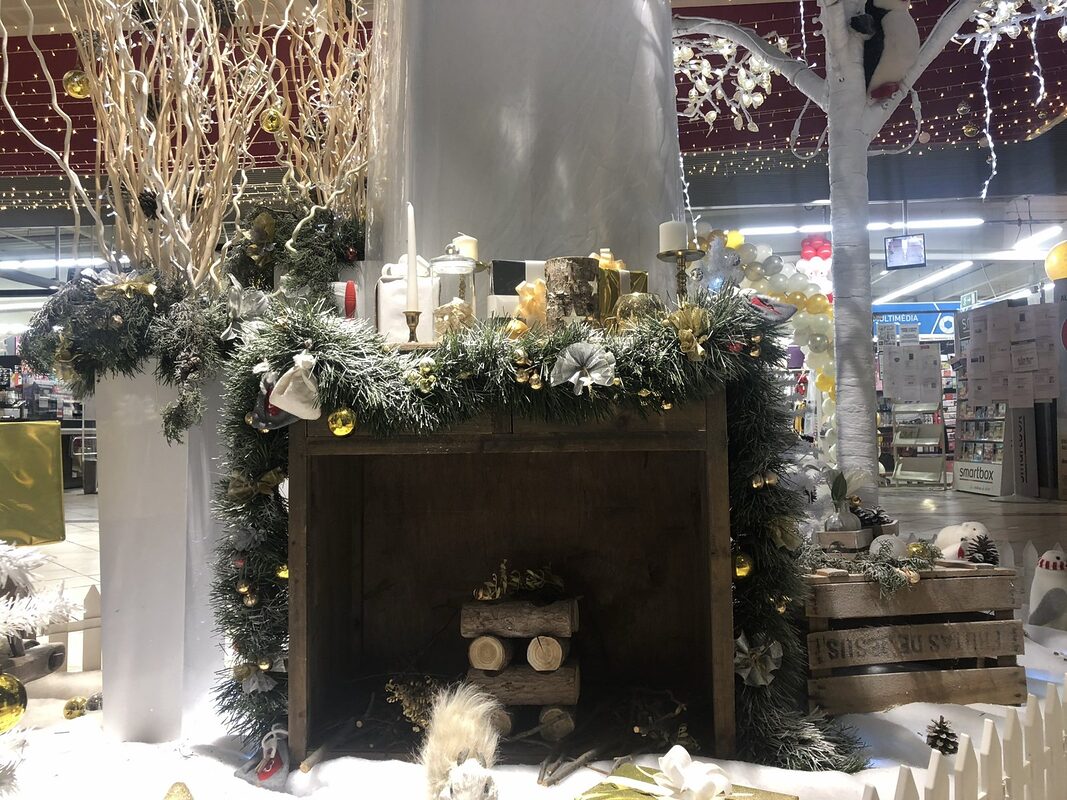 Fausse cheminée en bois habillée de guirlande de sapin, chandeliers dorés, bocaux et bûches, branches blanches et cagette en bois