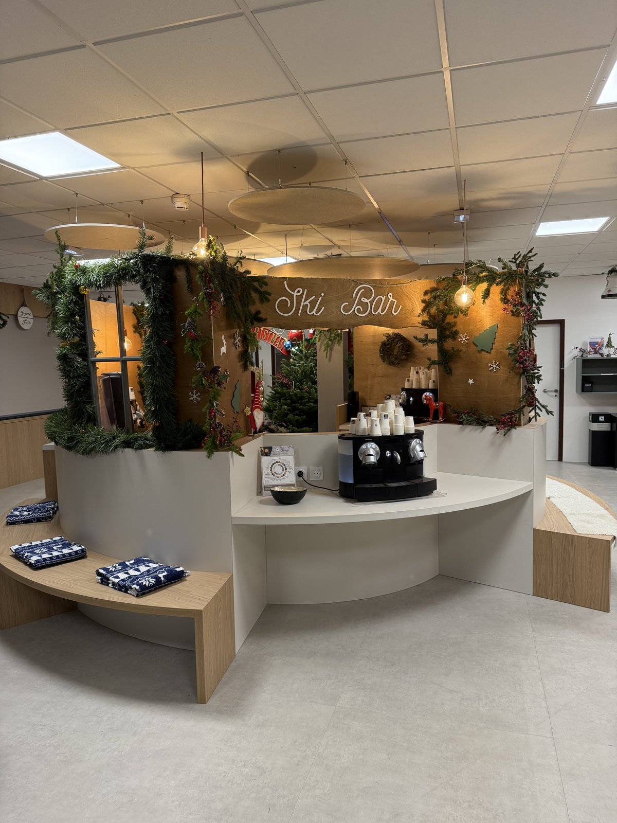 Comptoir café transformé en ski bar : enseigne en bois, guirlandes de sapin et de baies rouges, banquettes et plaids d’hiver