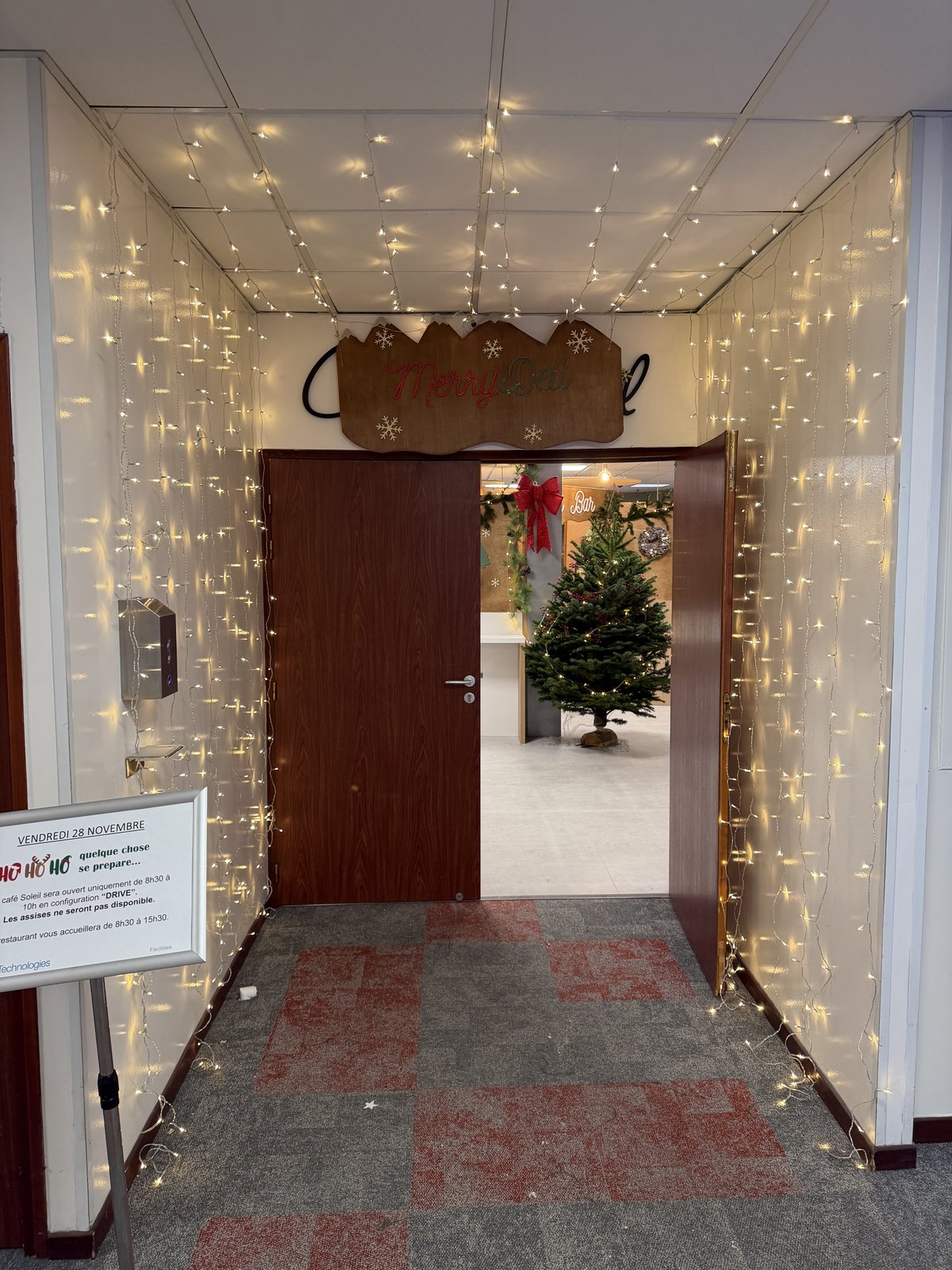 Couloir d’entrée tapissé de rideaux lumineux blanc chaud, enseigne en bois au-dessus de la porte et sapin de Noël au fond