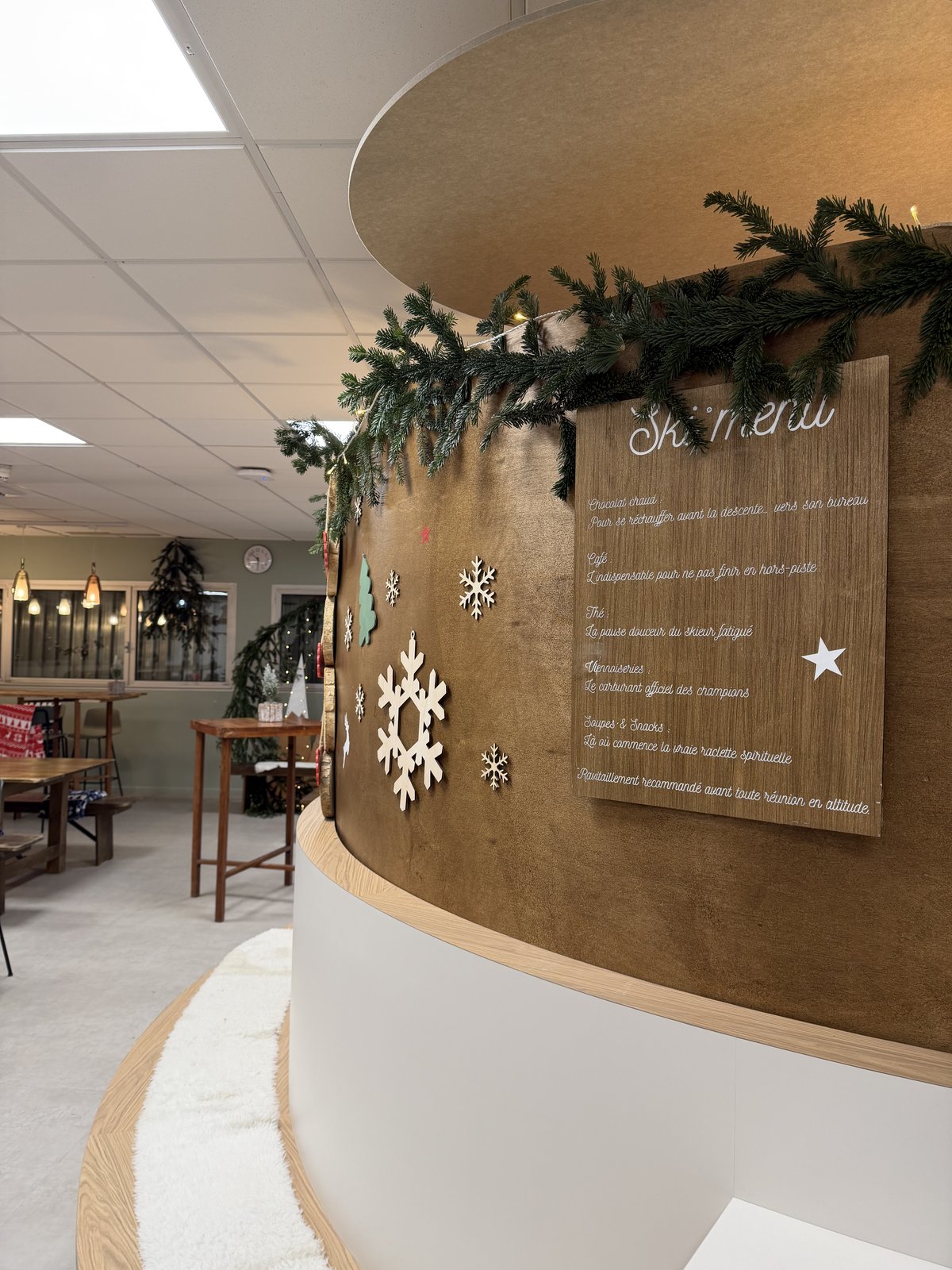 Mur arrondi en bois habillé d’une guirlande de sapin, de flocons blancs et d’un panneau de menu en bois façon chalet