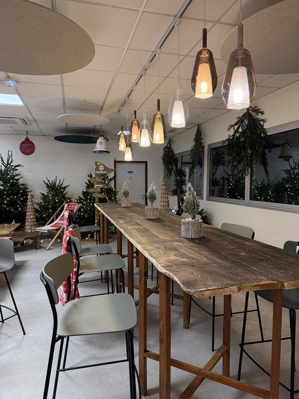 Noël d'entreprise esprit chalet : grande table haute en bois et tabourets dans un espace de restauration décoré de sapins