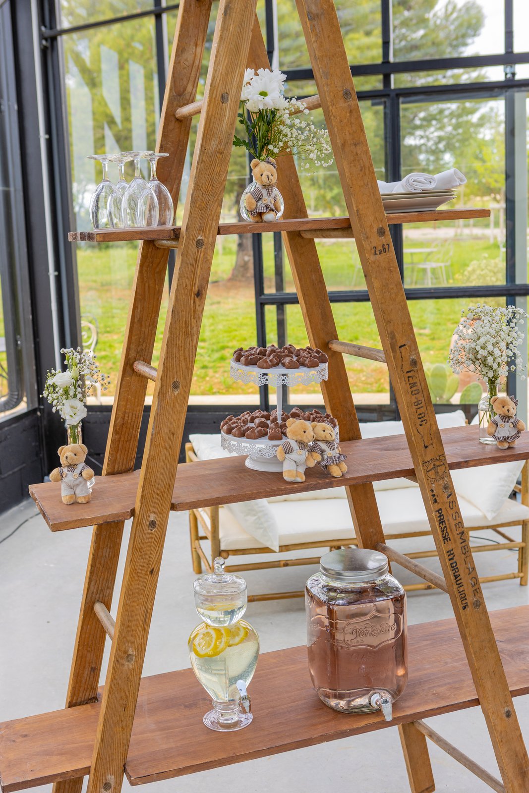 Échelle en bois à plateaux : verres, chocolats sur supports blancs, petits nounours, citronnade et bocal à robinet