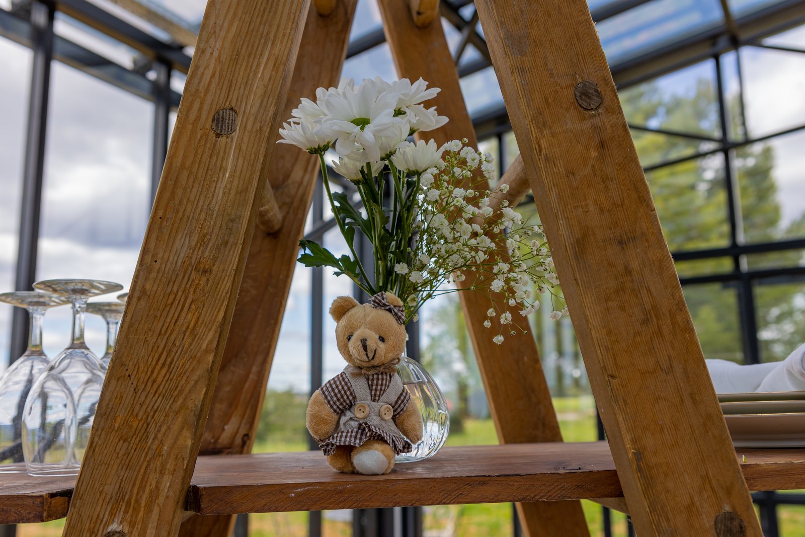 Petit nounours dans un vase boule garni de marguerites blanches et de gypsophile, sur une échelle en bois