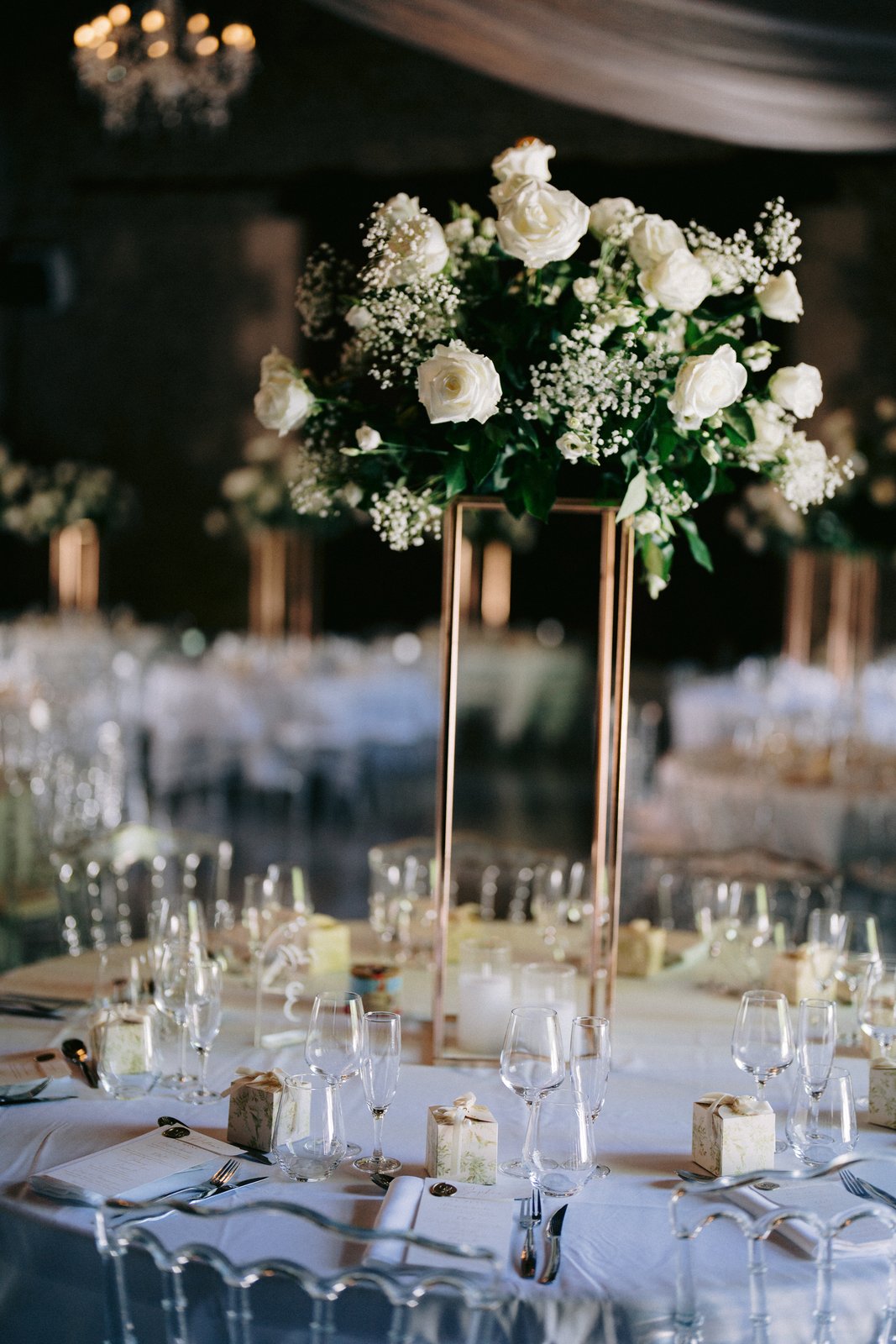 Composition de roses blanches et gypsophile sur un support doré, table ronde nappée de blanc et chaises transparentes