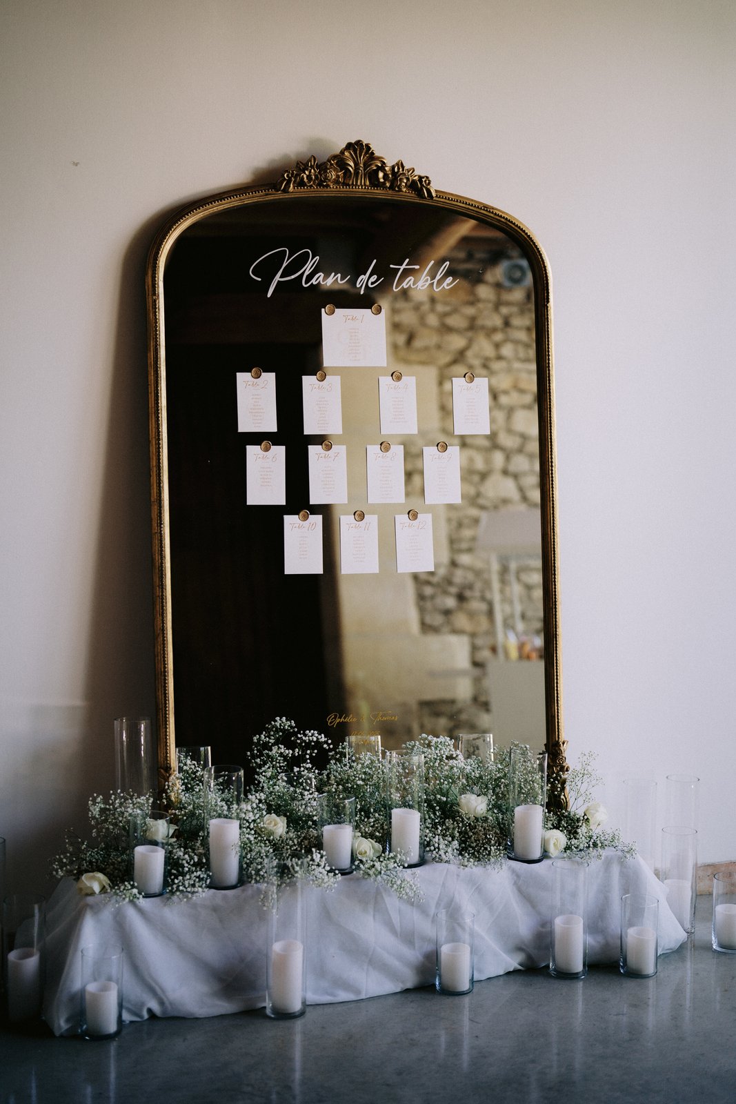 Plan de table sur un grand miroir à moulures dorées, gypsophile, roses blanches et bougies dans des vases cylindres