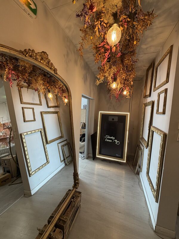 Couloir du showroom Pink Event : cadres dorés, grand miroir, suspension de fleurs séchées et borne photo miroir